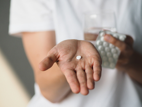 Health conscious person holding a variety of natural vitamins, supplements and herbal remedies, while their other hand holds a glass of water ready to take the pills.
