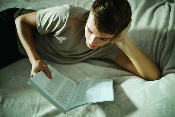 Teenage boy studying in bed