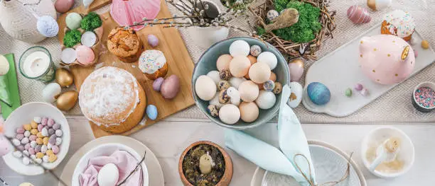 Table decoration for Easter celebration in kitchen.Tablescape for Easter holiday at home.Family religious traditional festive christianity,catholic meal food.Pop color eggs,cake,fun bunny,candy sweet.