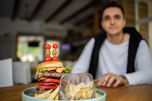 A young man is sitting in a restaurant and eating a big hamburger