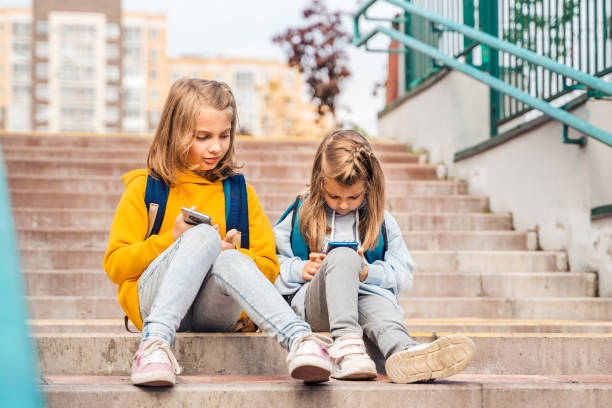 istock Back to elementary,primary school. Little girls with backpack,mobile phone.Chat, talk with mom,friends, classmates on break.Autumn study after vacation. Education of children.Pupil kid on stair steps 1430798858