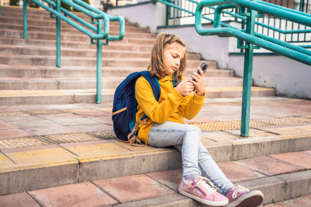 istock Back to elementary, primary school. Little girl with backpack,mobile phone. Chat, talk with friends, classmates on break. Autumn study after vacation. Education of children. Pupil kid on stair steps 1430798863