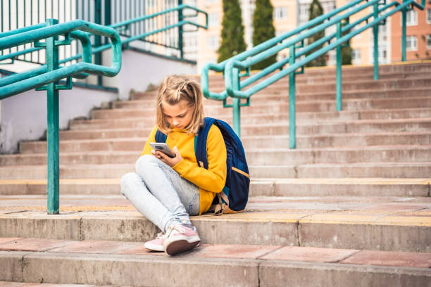 istock Back to elementary, primary school. Little girl with backpack,mobile phone. Chat, talk with friends, classmates on break. Autumn study after vacation. Education of children. Pupil kid on stair steps 1430798881