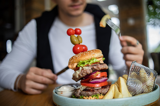 A young man is sitting in a restaurant and eating a big hamburger