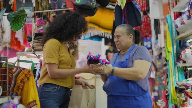 Mid adult woman buying mexican doll from senior saleswoman at a gift shop