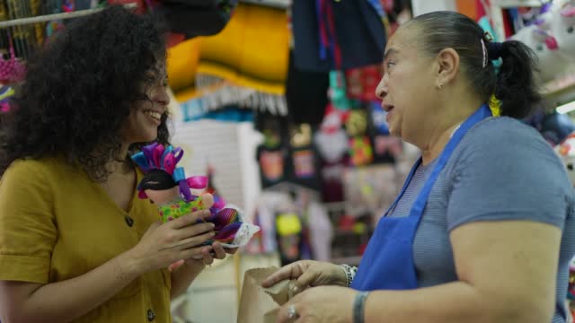 Mid adult woman buying mexican doll from senior saleswoman at a gift shop