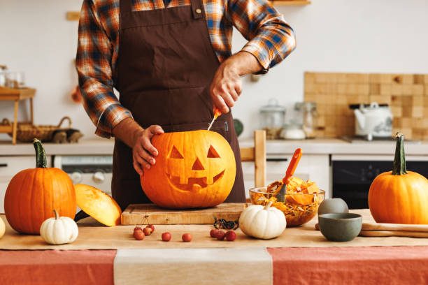 istock Man in apron standing in kitchen and carving large orange Halloween pumpkin 1430802749
