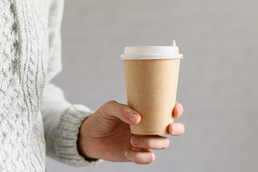 Close-up of a man holding a disposable paper cup with coffee in his hand. Selective focus on a cup, template.
