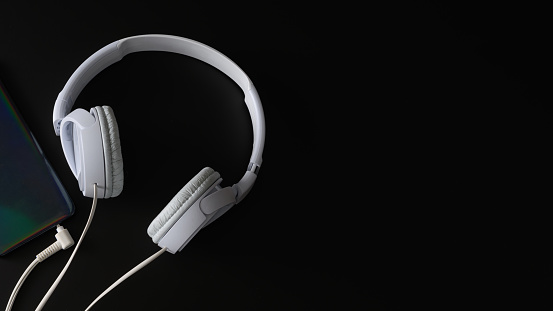 White headphones and part of smartphone on a black background. Horizontal banner