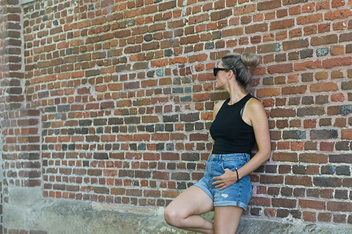 Beautiful young woman in summer clothes in profile against the background of a brick wall. copy space