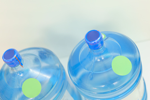 The top of two plastic gallon water bottle containers with green round labels stand on a blue background. Healthy. Object. Transparent. Clear. Bottled. Cooler. Freshness. Mineral. Background