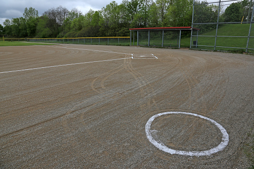 The on deck circle of an unoccupied baseball field on a cloudy day.