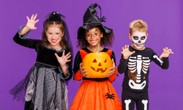 istock Happy Halloween! Kids in carnival costumes and makeup make a terrible gesture on bright colored purple background 1430811237