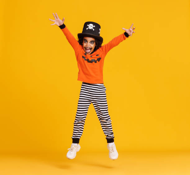 glücklicher ethnischer junge im kürbiskostüm springt und feiert halloween auf gelbem hintergrund - child jumping vegetable food stock-fotos und bilder