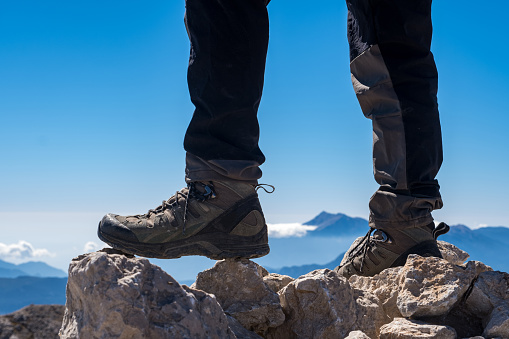 Mountainous region at high altitudes. Mountain landscape model steps on the rocks at the summit with outdoor shoes. The feet are clear and the background is out of focus. Outdoor mountain peak cloudy nature landscape