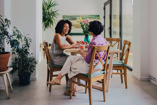 A beautiful Latin-American woman smiling while sitting at the table and talking to her anonymous Latin-American friend. (diverse friends)