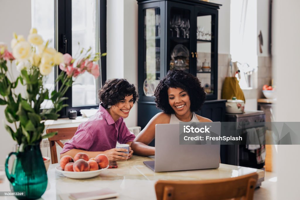 Two Happy Businesswomen Working Together From Home On Their Comp A beautiful Latin-American entrepreneur smiling while watching something on her laptop with her friend. (diverse friends) Mentorship Stock Photo