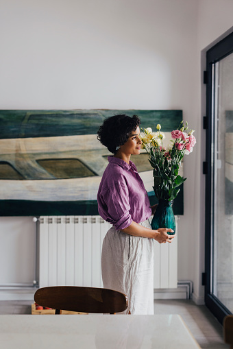 A side view of a beautiful smiling Latin-American woman looking away while holding a vase of flowers.