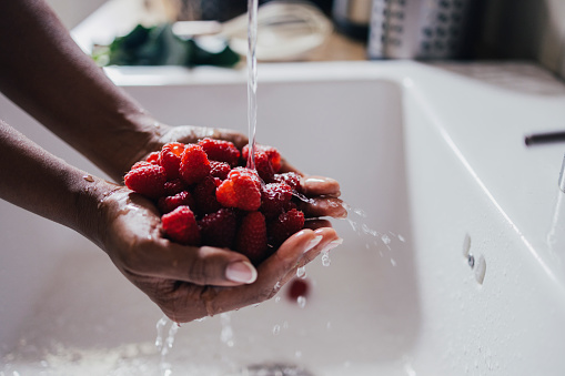 A Side View Of An Unrecognizable Woman Washing Raspberries