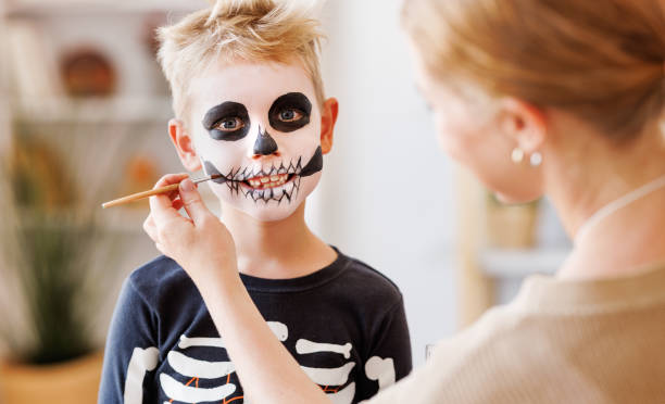 istock Festive makeup for Halloween. Woman doing skeleton make-up for boy in costume while preparing holiday 1430813672