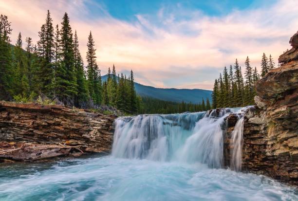 Sunrise Sky Glowing Over Sheep River Falls A view of water rushing at Sheep River Falls under a colourful sunrise sky in the summer. kananaskis country stock pictures, royalty-free photos & images