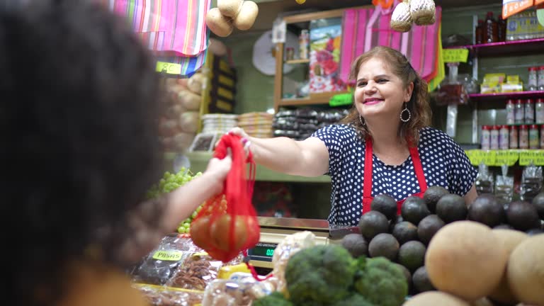 Mature woman handing products to customer at local market