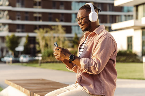 istock A smiling man using mobile phone and wireless headphones outdoors 1430817268