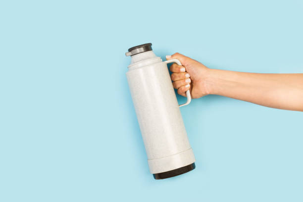 istock Woman hand holding a gray thermo bottle on a light blue background 1430830548