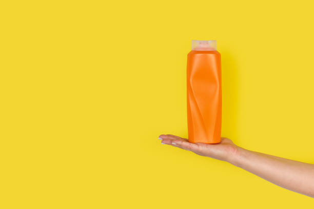 istock Woman hand holding a shampoo bottle on a yellow background 1430830592