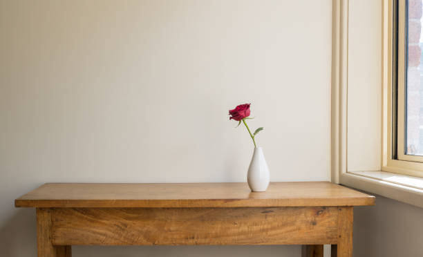 istock Single red rose in white vase on oak side table against beige wall 1430841453