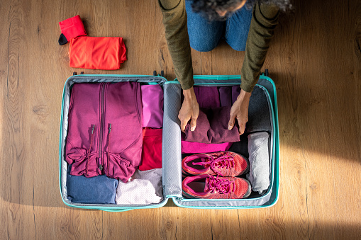 Woman packing pink sportswear in suitcase, high angle view, trekking adventure preparation. Folded female clothes in open luggage, hiking planning