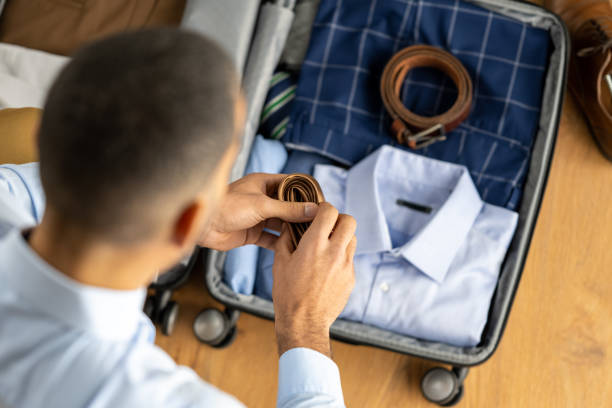 Man packing suitcase for business travel, folded formalwear in luggage, top view stock photo