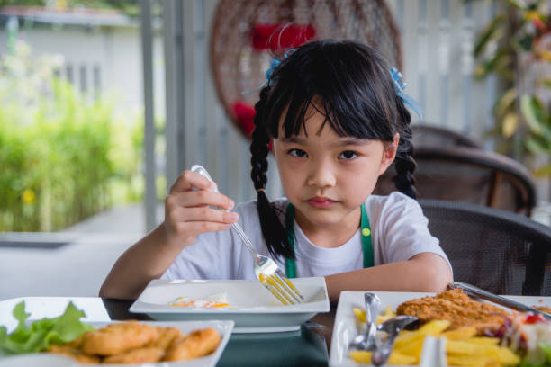 istock little girl asian eat fried egg on dish at table. 1430846623