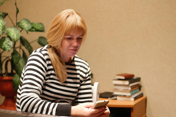 Defocus serious charming woman using smartphone while working at home. Young french blonde woman with ponytail. Reading news. Out of focus.