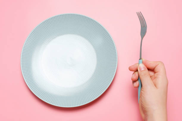 istock Empty plate and female hand with fork on pink background close-up top view. 1430849707