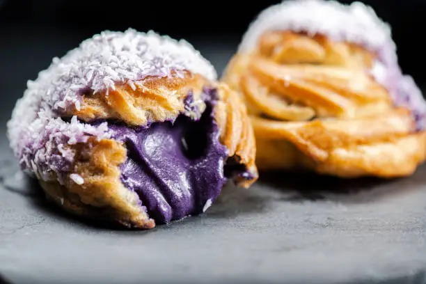 Home made ube cream puff with purple coloured white chocolate and coconut, also known as a Profiterole.