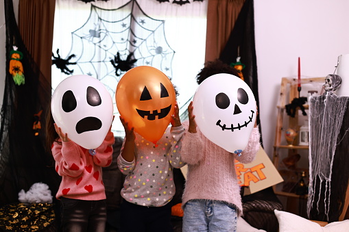 Children or little kids celebrating Halloween at home kitchen, Children hold Halloween Balloon hid their face , Funny child girl in Halloween  costume