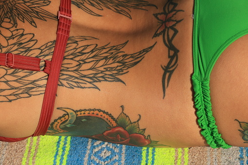 A Native woman lying face down on a towel. She is wearing a red bikini top and green bottom on a blue and yellow pattern towel.