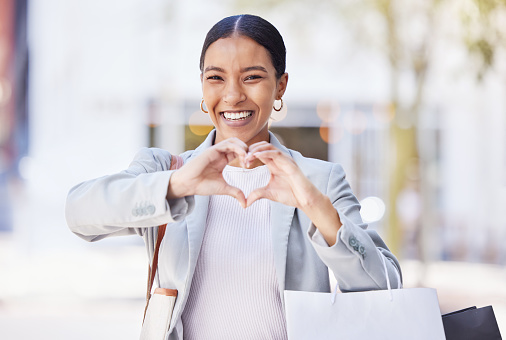 Shopping woman with love and heart sign or hand in an urban city street with retail bags. Professional fashion business female, customer and designer with self care or emoji hands, portrait and smile