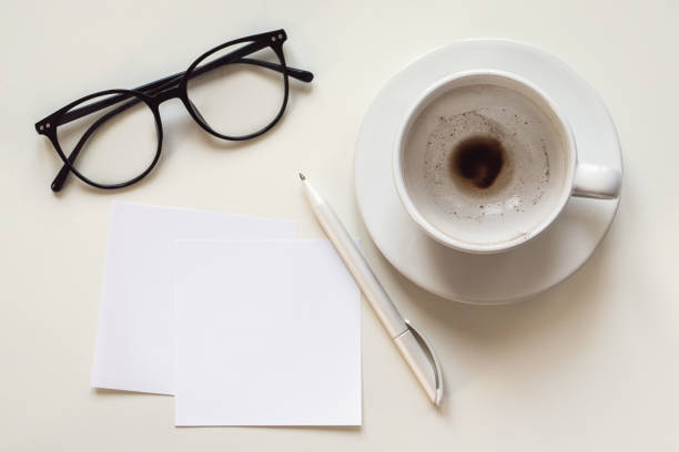 istock Paper notes mockup, blank space, empty coffee cup, eyeglasses and pen on white desk, overhead flat lay 1430880302