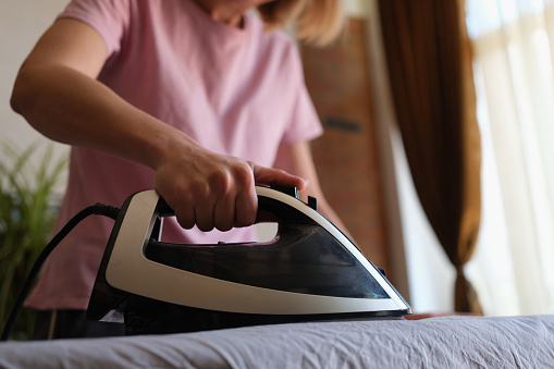 Woman ironing clothes on board at home closeup. Proper ironing concept