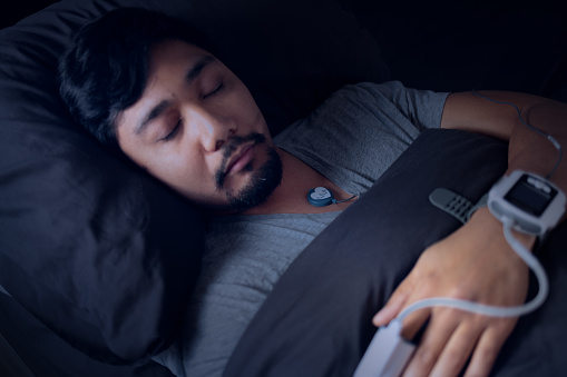 Asian Man Wearing a Pulse Oximeter in Bed - At Home Sleep Study Test for Sleep Apnea - Blood Oxygen Saturation Monitor - Sleep Hypoxia - Disrupted REM Sleep - Daytime Sleepiness and Fatigue 
Shot with Canon R5