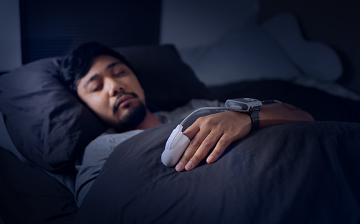 Asian Man Wearing a Pulse Oximeter in Bed - At Home Sleep Study Test for Sleep Apnea - Blood Oxygen Saturation Monitor - Sleep Hypoxia - Disrupted REM Sleep - Daytime Sleepiness and Fatigue 
Shot with Canon R5