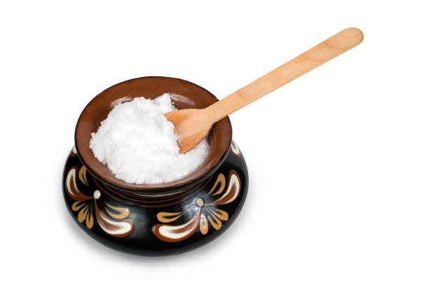 Table salt with a wooden spoon in a ceramic pot. Clay pot with salt on a white background.