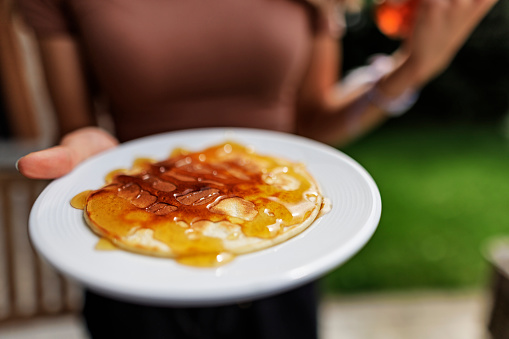Teenage girl holding a plate with a pancake, The girl has topped the pancake with honey.
Canon R5