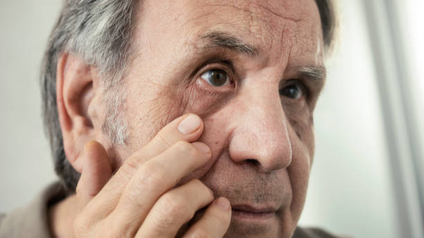 istock Old man examines his own eye in the mirror 1430896443