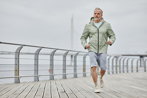 Minimal full length portrait of handsome mature man running towards camera outdoors by river, copy space