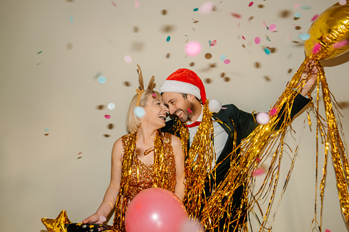 Photo of a smiling couple celebrating New Year's Eve, while colourful confetti falling over during countdown