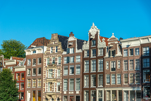 CLOSE UP: Gorgeous 17th century slim and high canal houses along Amsterdam waterway opened as museums, offices and hotels. Famous buildings with historic facades, skinny profile and grand gables