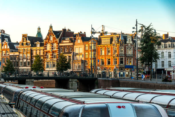 Typical canal in the center of Amsterdam. Early morning. Visible are sightseeing tourism boats at canal (gracht) waterfront and many typical dutch houses in raw . Amsterdam, Netherlands.